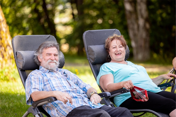 Zwei Patienten sitzen draußen im Grünen auf Liegestühlen und lächeln.