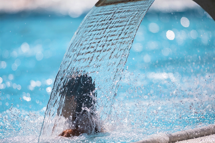 Rückansicht einer Person, die in einem Schwimmbecken unter einer Wasserfontäne steht.