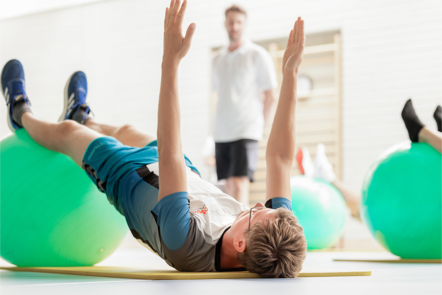 Ein Patient liegt mit den Beinen auf einem Gymnastikball auf dem Boden.